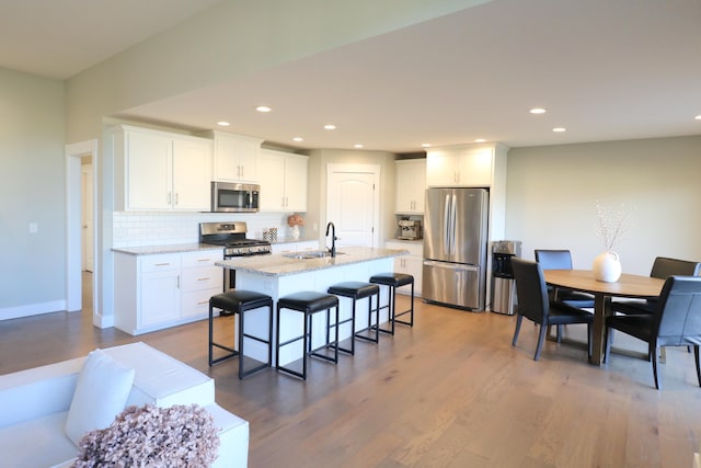 1224 S Mulberry Ave, Springfield, MO 65802 - kitchen with stainless steel appliances, decorative backsplash, a breakfast bar area, white cabinetry, and an island with sink