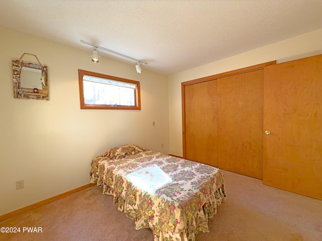 carpeted bedroom with a textured ceiling, rail lighting, and a closet