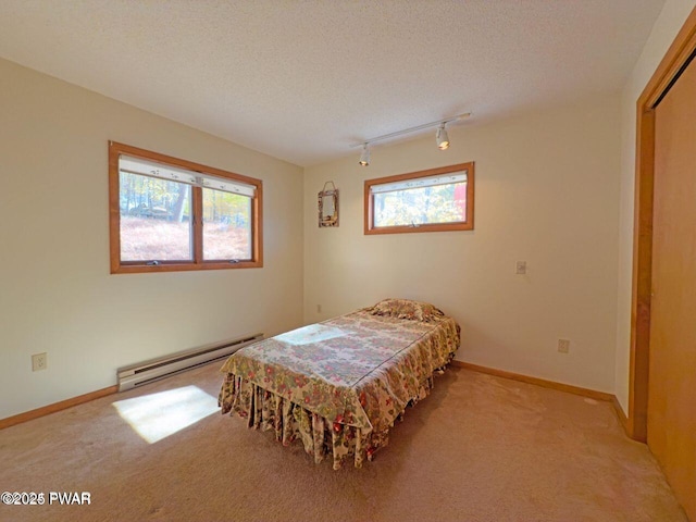 bedroom featuring a baseboard heating unit, rail lighting, multiple windows, and carpet