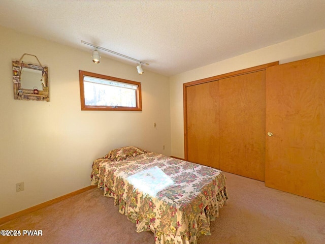 carpeted bedroom with rail lighting, a textured ceiling, and a closet