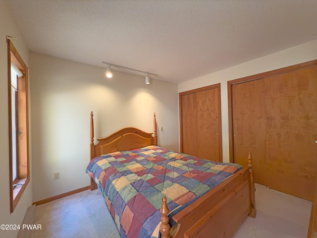 carpeted bedroom with two closets, a textured ceiling, and track lighting