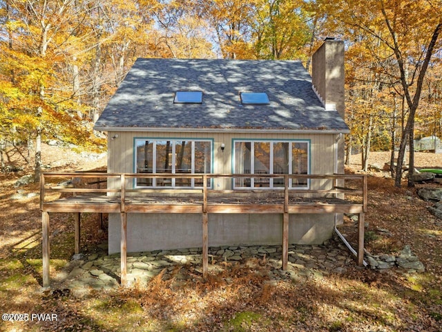 rear view of house featuring a chimney, a deck, and roof with shingles