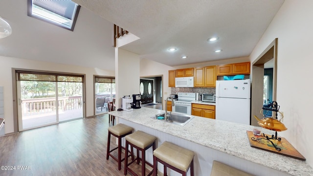 kitchen with a breakfast bar, white appliances, backsplash, sink, and light stone countertops