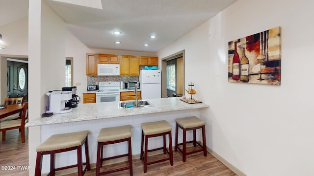 kitchen featuring kitchen peninsula, backsplash, white appliances, sink, and light hardwood / wood-style flooring