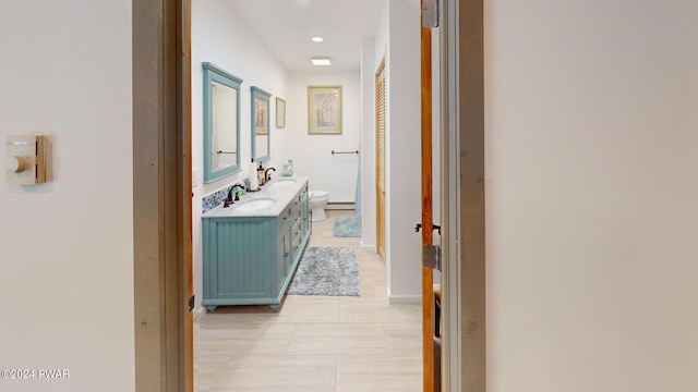 hall featuring light tile patterned floors, baseboard heating, and sink