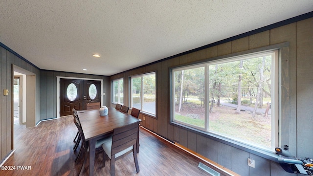 dining space featuring wood walls, a healthy amount of sunlight, a textured ceiling, and wood-type flooring