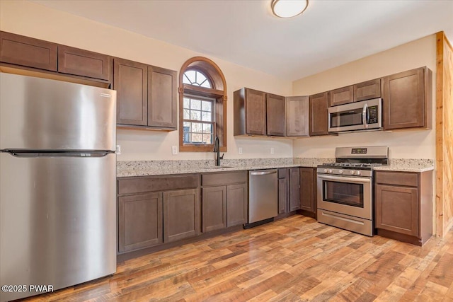 kitchen with a sink, light stone counters, light wood-type flooring, and stainless steel appliances