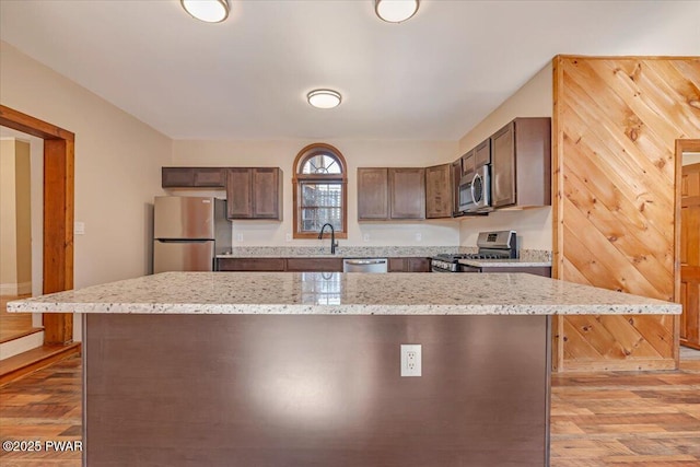 kitchen with a sink, light stone counters, light wood-style floors, and stainless steel appliances