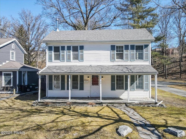 traditional-style home featuring covered porch, a front yard, and a shingled roof