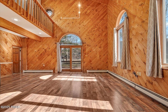 unfurnished living room with wooden walls, a baseboard heating unit, baseboard heating, a towering ceiling, and hardwood / wood-style flooring