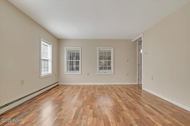 unfurnished room featuring baseboard heating, light wood-style flooring, and baseboards