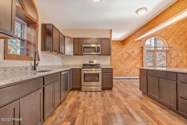 kitchen featuring a baseboard radiator, light wood-style flooring, a sink, wood walls, and appliances with stainless steel finishes