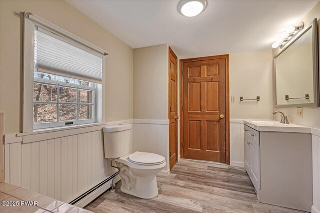 bathroom with toilet, wainscoting, wood finished floors, vanity, and a baseboard radiator