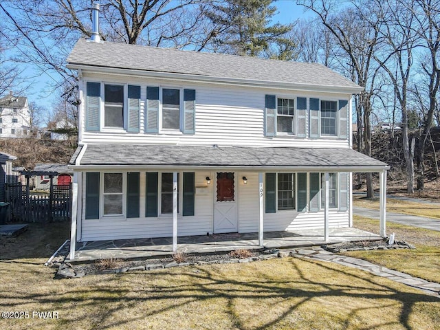 view of front of home featuring roof with shingles, covered porch, and a front yard