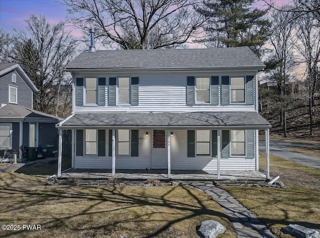 traditional-style house featuring a porch, a yard, and a shingled roof