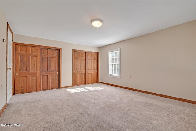 unfurnished bedroom featuring baseboards, multiple closets, and carpet floors