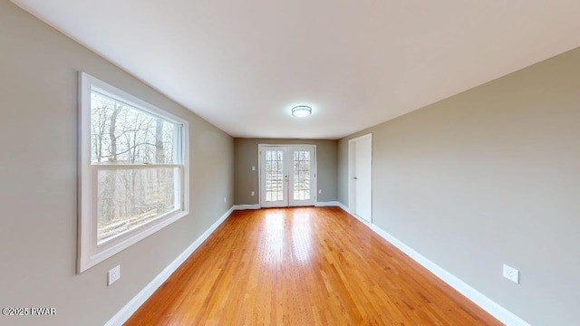 empty room with light wood-style floors, french doors, and baseboards