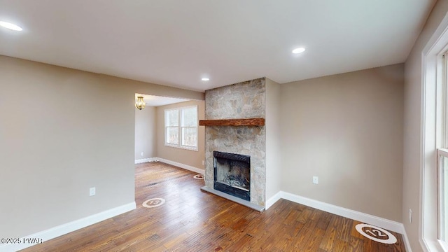 unfurnished living room with recessed lighting, a large fireplace, baseboards, and wood finished floors