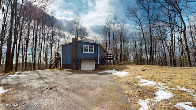 exterior space featuring an attached garage, aphalt driveway, stairway, and a chimney