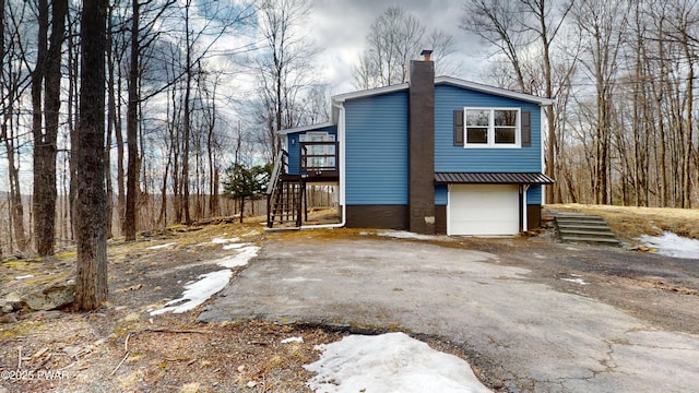 view of home's exterior featuring an attached garage, a chimney, stairway, and aphalt driveway