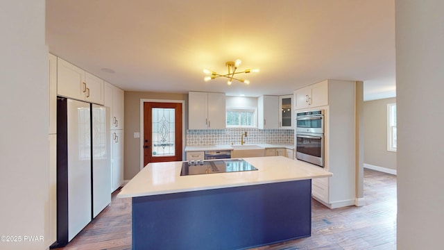 kitchen featuring tasteful backsplash, freestanding refrigerator, black electric stovetop, stainless steel double oven, and white cabinetry