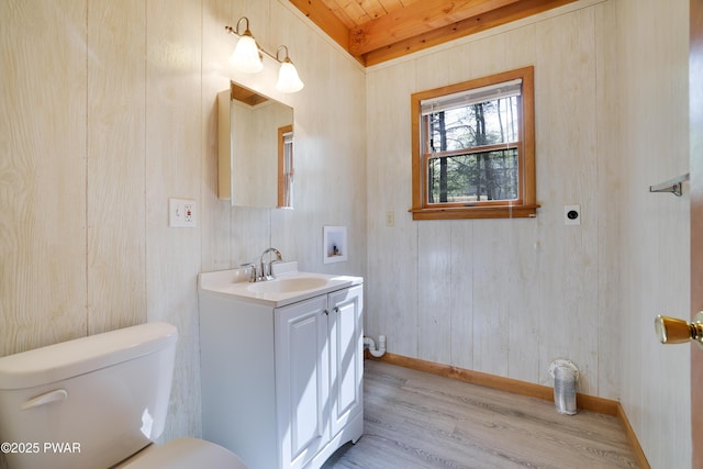 bathroom featuring wood finished floors, toilet, baseboards, vanity, and beam ceiling