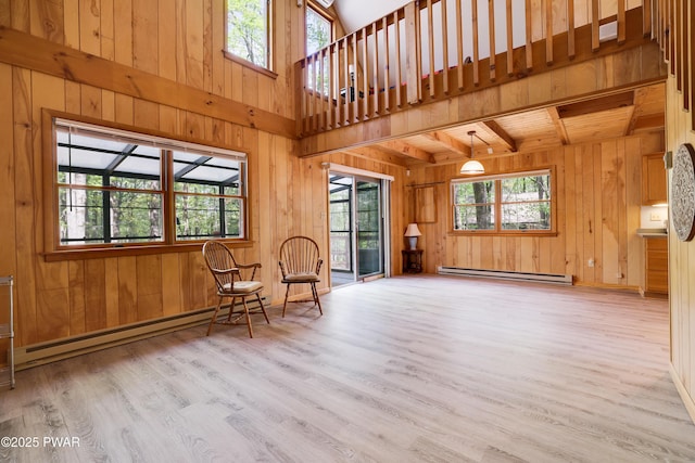living area featuring baseboard heating, wood walls, wood finished floors, beam ceiling, and a high ceiling