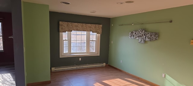 spare room featuring baseboard heating, baseboards, visible vents, and wood finished floors