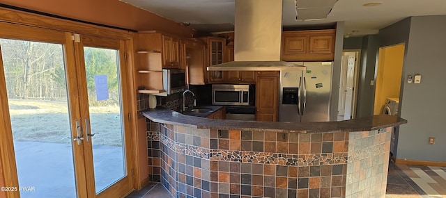 kitchen featuring a peninsula, island exhaust hood, a sink, stainless steel appliances, and brown cabinets