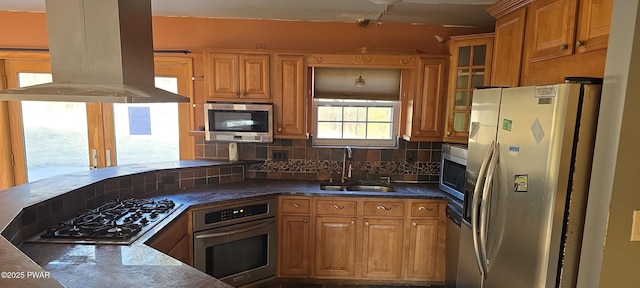 kitchen with glass insert cabinets, decorative backsplash, appliances with stainless steel finishes, island range hood, and a sink