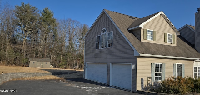 view of side of home with an outbuilding, an attached garage, driveway, and a shingled roof