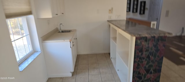 kitchen featuring baseboards, light countertops, light tile patterned floors, white cabinets, and a sink