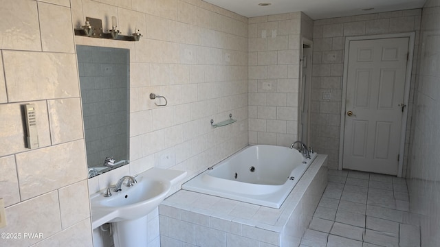 bathroom with tile patterned floors, a tub with jets, tile walls, and a sink