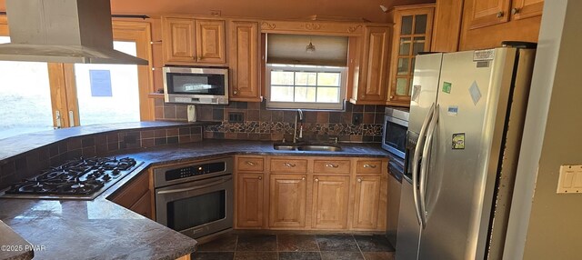 kitchen with island exhaust hood, a sink, decorative backsplash, glass insert cabinets, and appliances with stainless steel finishes