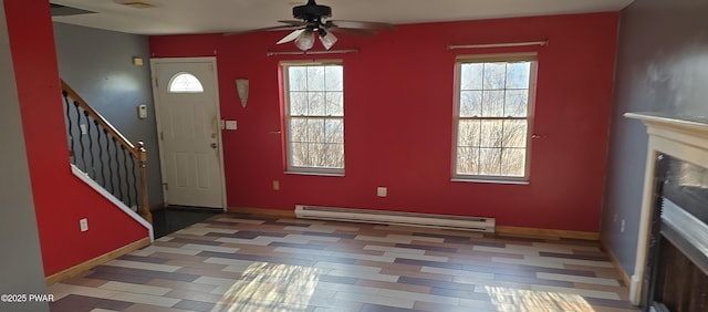 foyer entrance with stairway, baseboard heating, a healthy amount of sunlight, and a ceiling fan