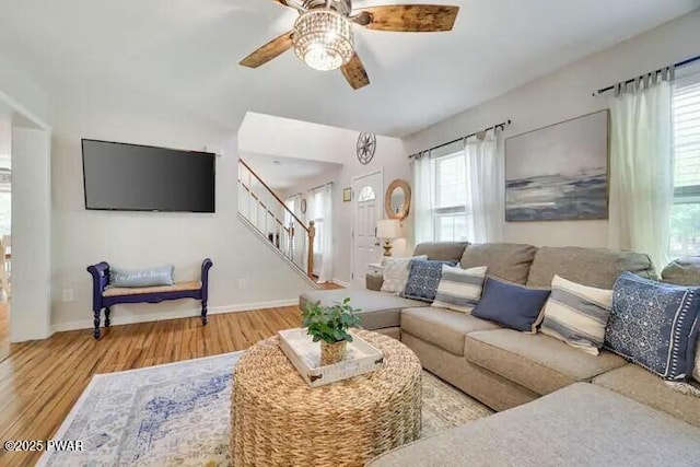 living area with ceiling fan, baseboards, wood finished floors, and stairs