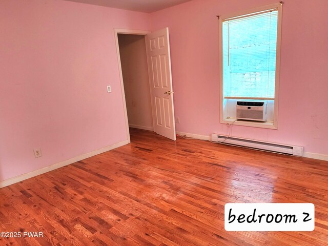 empty room with cooling unit, light wood-type flooring, and a baseboard heating unit