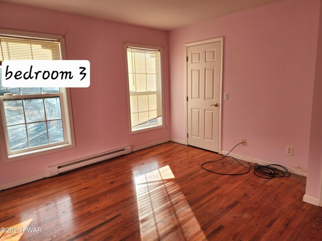 empty room featuring hardwood / wood-style floors and a baseboard heating unit