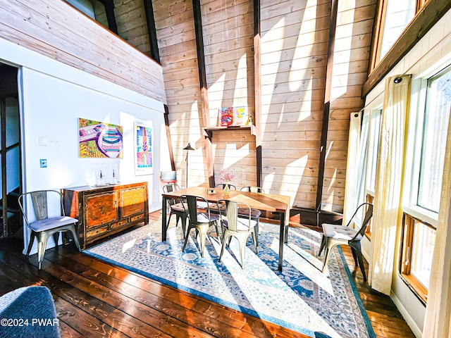 dining room with dark hardwood / wood-style floors, wood walls, and high vaulted ceiling