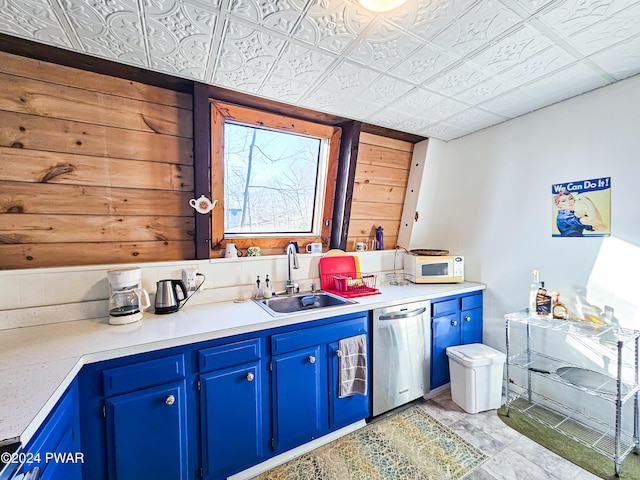 kitchen featuring blue cabinetry, stainless steel dishwasher, wooden walls, and sink