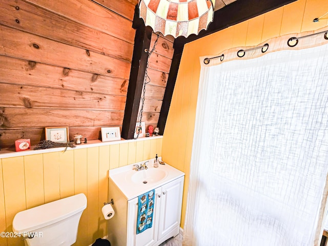 bathroom with vanity, toilet, and wood walls