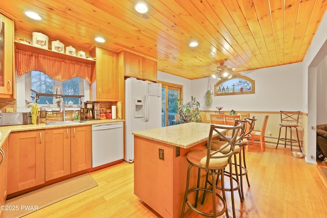 kitchen featuring light stone countertops, white appliances, a kitchen island, sink, and light wood-type flooring