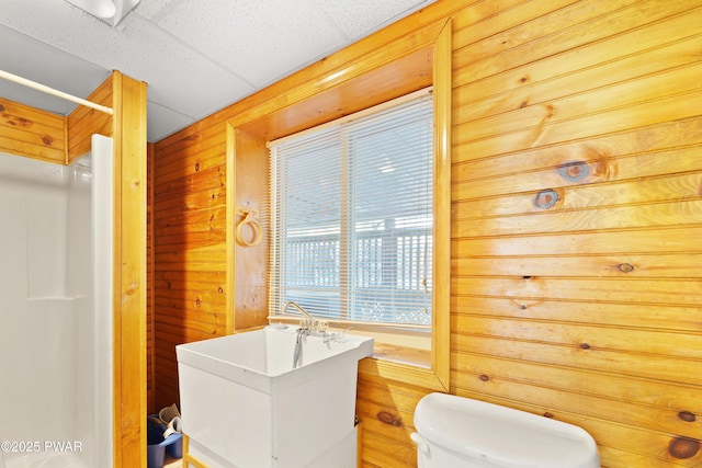 bathroom with a drop ceiling, toilet, and wooden walls