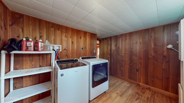 laundry room featuring wooden walls, washing machine and clothes dryer, and light wood-type flooring