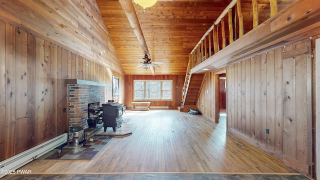 unfurnished living room featuring wood walls, wood-type flooring, wooden ceiling, baseboard heating, and ceiling fan