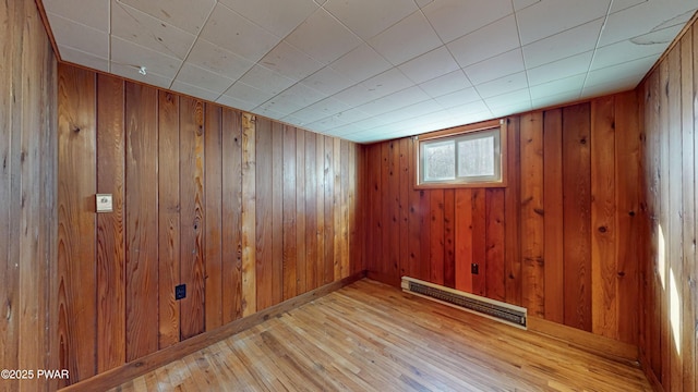 empty room featuring a baseboard heating unit, light hardwood / wood-style flooring, and wooden walls