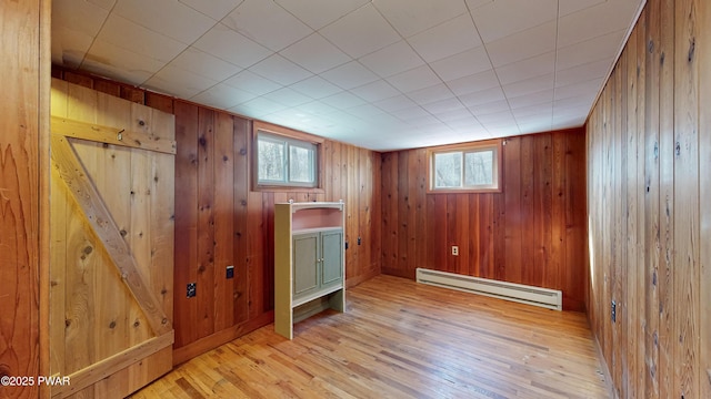 interior space featuring a baseboard radiator, wooden walls, light hardwood / wood-style floors, and a wealth of natural light