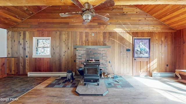 living room featuring lofted ceiling, a wood stove, ceiling fan, a baseboard heating unit, and wood walls