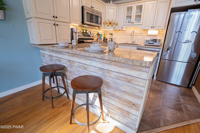 kitchen with tasteful backsplash, appliances with stainless steel finishes, glass insert cabinets, a sink, and a kitchen bar