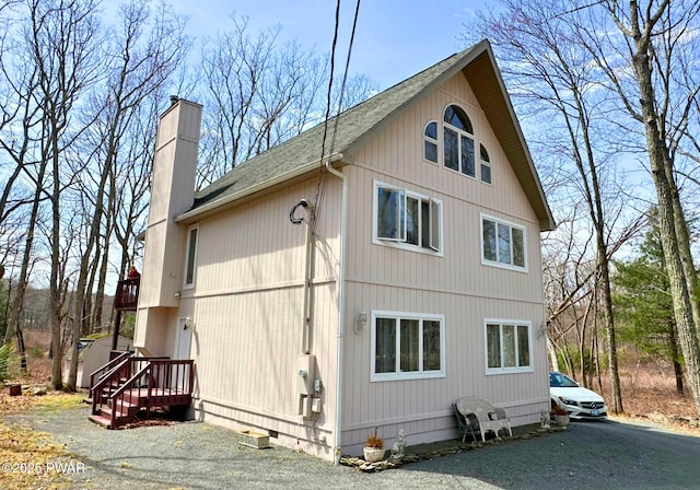 view of side of property with a shingled roof, aphalt driveway, and a chimney